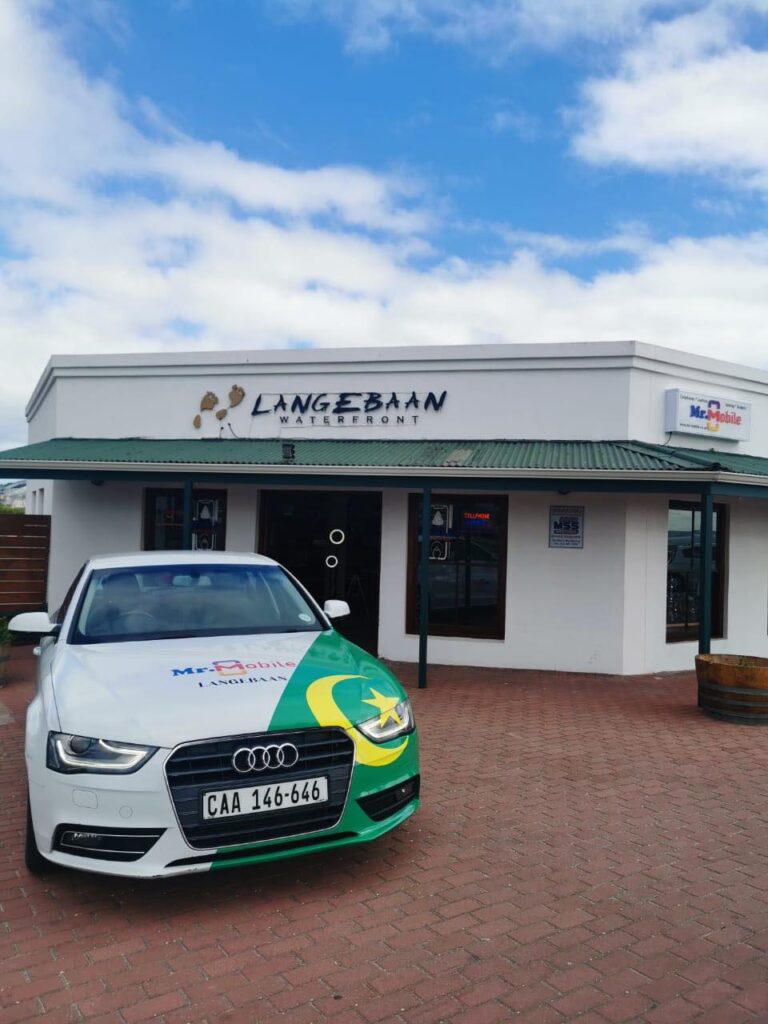 White Audi with green-yellow livery parked in front of a white Langebaan Waterfront storefront.